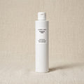 A white cylindrical bottle of Comfort Zone Essential Toner with black text, standing upright on a textured beige fabric background.