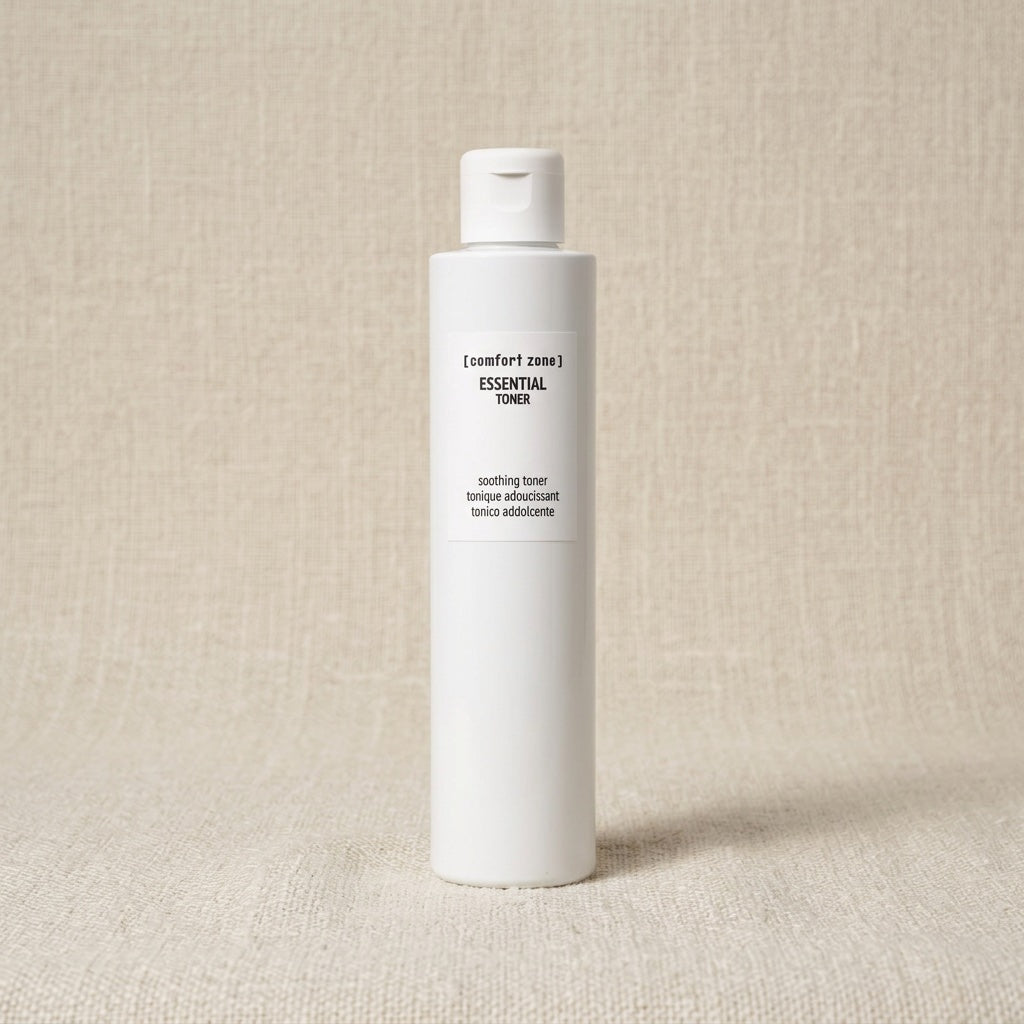 A white cylindrical bottle of Comfort Zone Essential Toner with black text, standing upright on a textured beige fabric background.