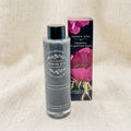A bottle of French Girl Charcoal Clarifying Wash with a black cap stands next to its retail box on a beige linen background. The bottle contains a gray cleanser, and the box features a black background with large pink flowers.