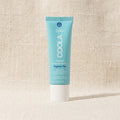 A tube of COOLA Classic Face Sunscreen, Foghose-Free, SPF 50, standing upright on a textured beige fabric background.