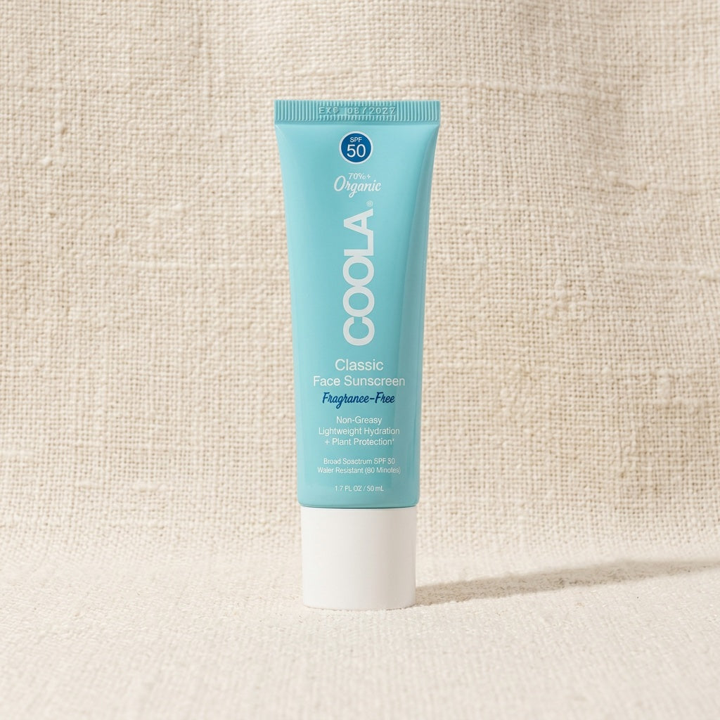 A tube of COOLA Classic Face Sunscreen, Foghose-Free, SPF 50, standing upright on a textured beige fabric background.