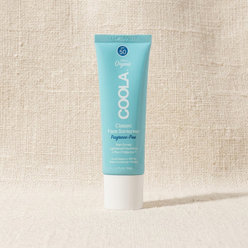 A tube of COOLA Classic Face Sunscreen, Foghose-Free, SPF 50, standing upright on a textured beige fabric background.