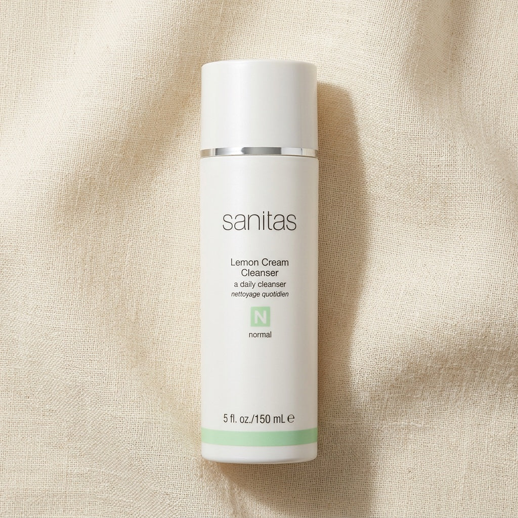 A white bottle of Sanitas Lemon Cream Cleanser with a silver band and a light green accent, set against a textured beige linen background.
