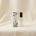 A bottle of French Girl Botanicals Nydia Blossom Facial Mist next to its illustrated packaging box, set against a draped cream linen fabric background.