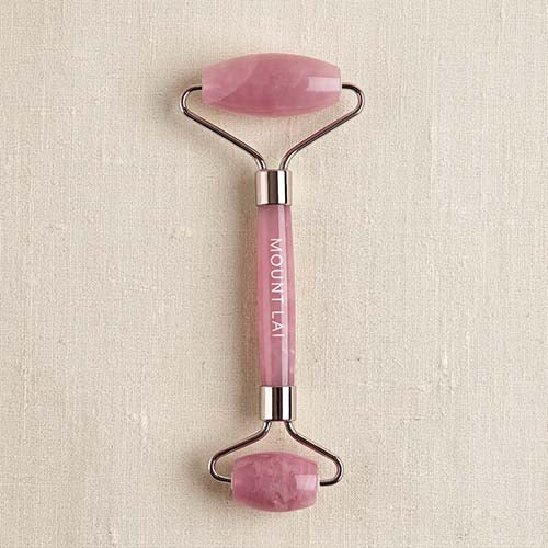 A pink rose quartz double-ended facial roller with a silver metal frame and the brand name 'MOUNT LAI' printed vertically on the handle, set against a textured beige background.