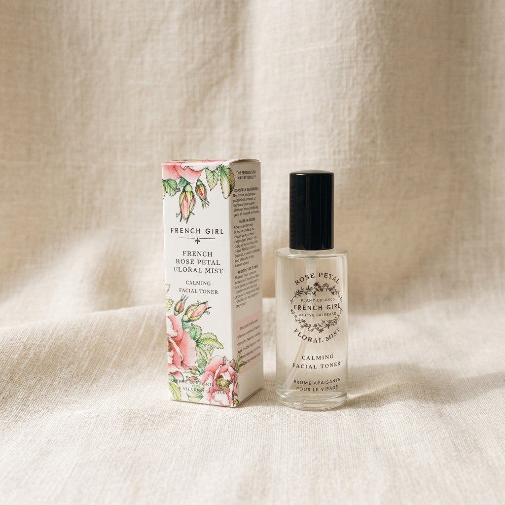 A bottle of French Girl Rose Petal Calming Facial Toner next to its floral illustrated packaging box, set on a neutral beige fabric background.