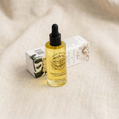 Rose Nectar French Gold Pure Facial Cleansing Oil in a clear glass dropper bottle with yellow oil, shown next to its white floral box on a beige linen background.